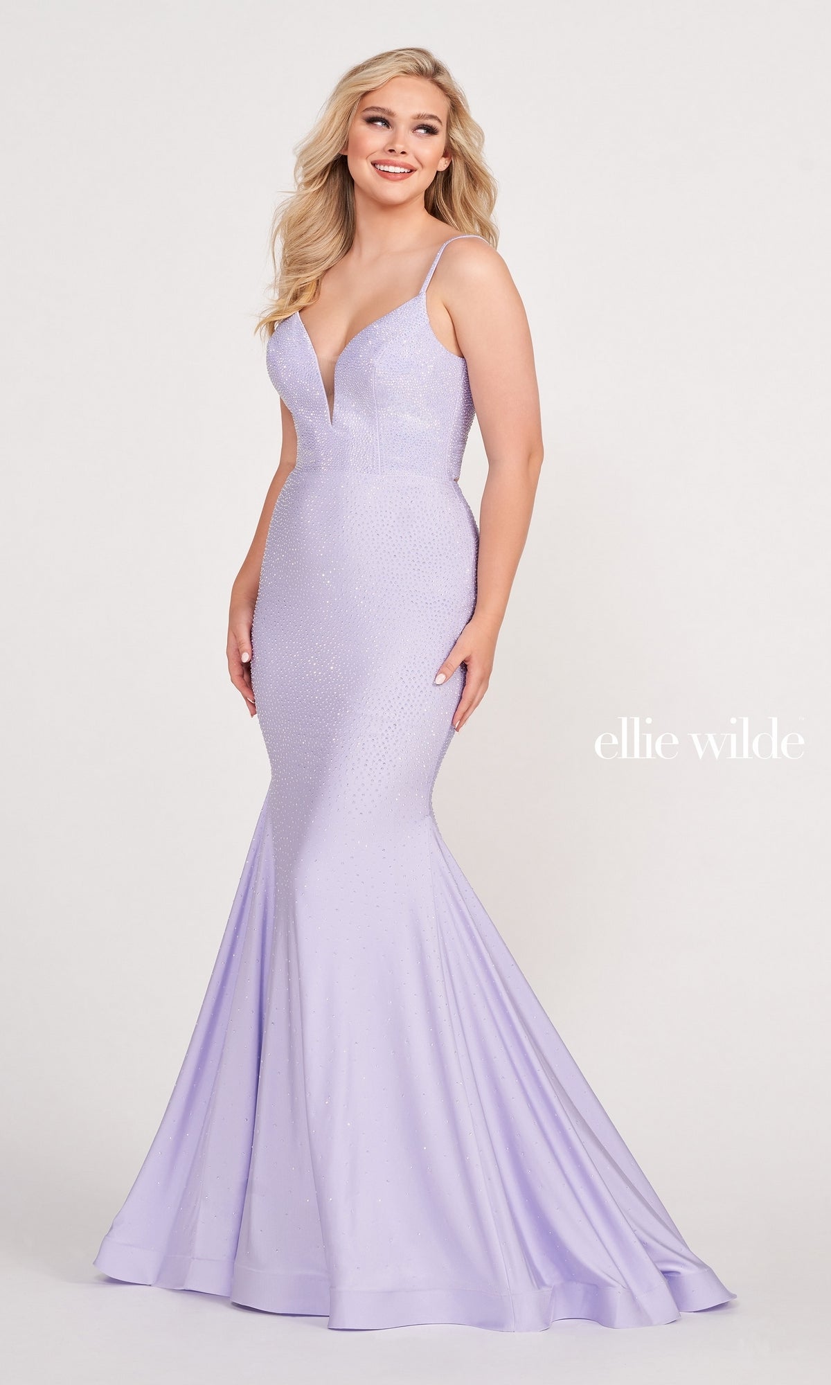 A woman wears the Ellie Wilde Beaded Mermaid Prom Dress with Cut Out, a light purple, floor-length gown featuring thin straps, subtle sparkles, and a v-neckline. The